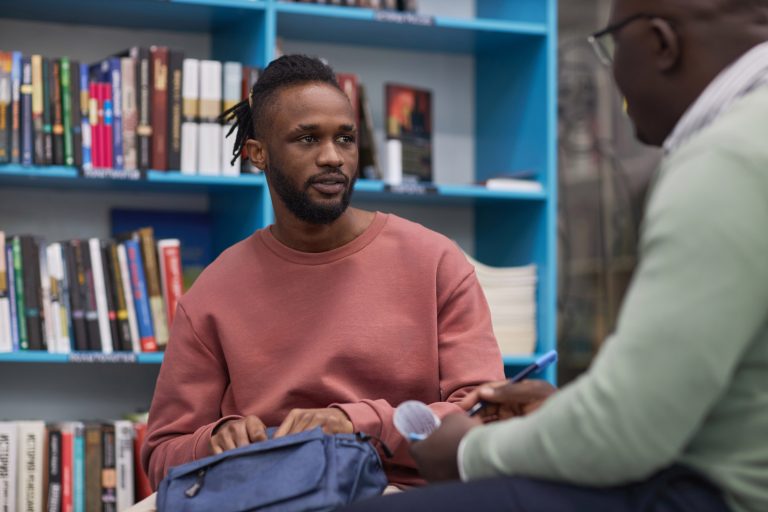 Jonge man praat met docent/begeleider in schoolbibliotheek