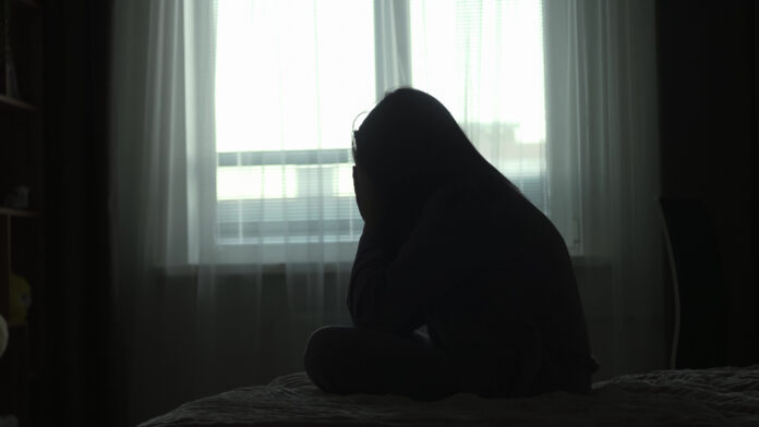 Silhouette of a millennial woman sitting on bed in the dark bedroom, depression, pain. Portrait of Unhappy sad woman sitting against window and thinking about her life Silhouette of a millennial woman sitting on a bed in the dark bedroom, depression, pain. Portrait of Unhappy sad woman sitting against window and thinking about her life