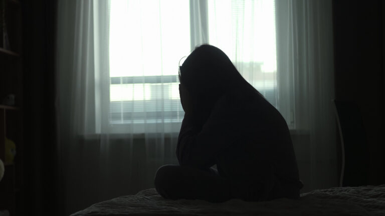 Schade erkennen Silhouette of a millennial woman sitting on a bed in the dark bedroom, depression, pain. Portrait of Unhappy sad woman sitting against window and thinking about her life